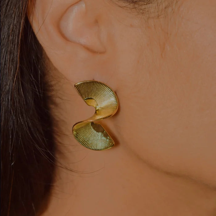 Gold earrings worn by a person with a blurred background