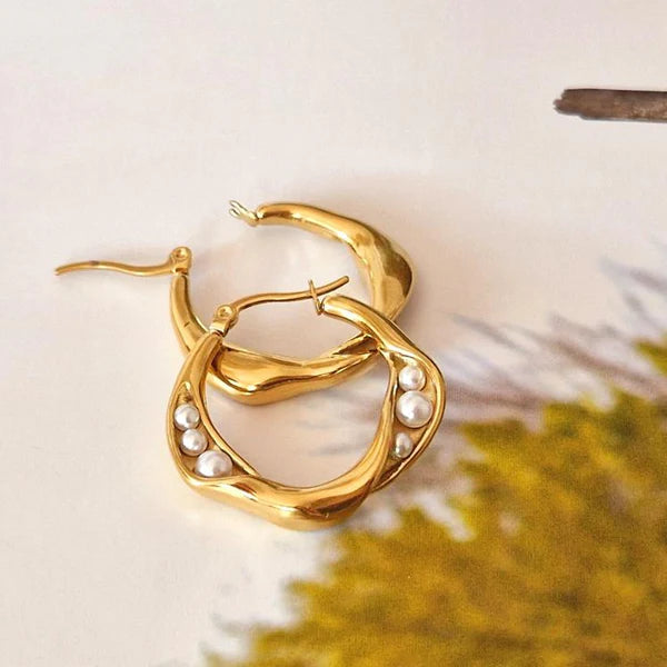 Gold hoop earrings with elegant pearl accents placed on surface, blending luxury with classic charm for modern style.