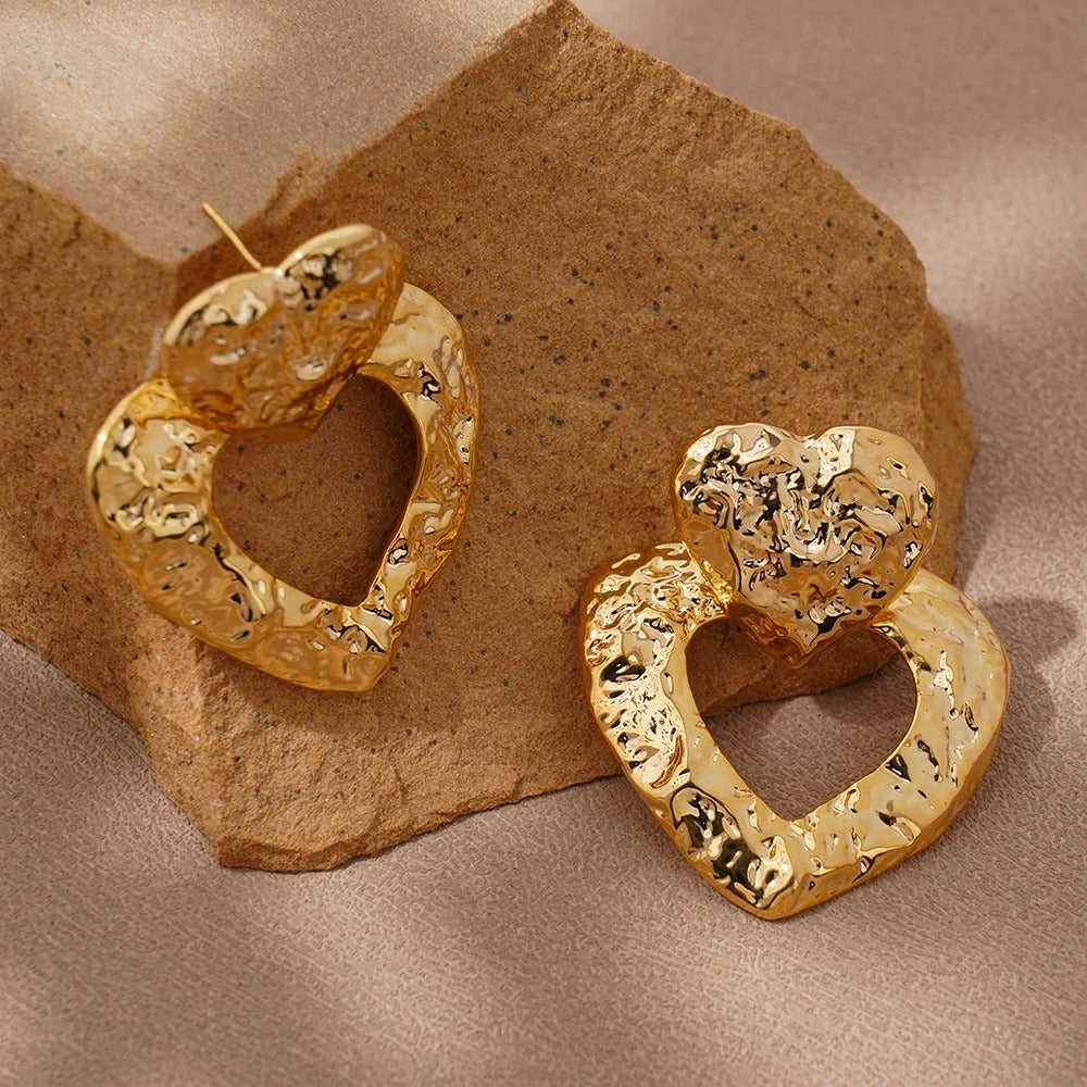 Gold heart-shaped earrings on a textured beige surface