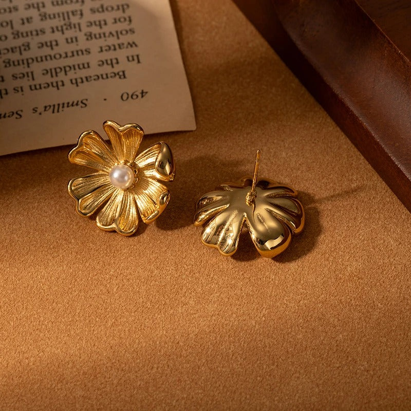 Gold flower-shaped earrings on a textured surface with a book in the background
