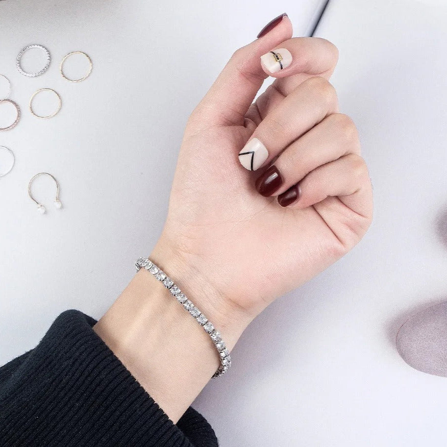Stylish silver tennis bracelet with sparkling stones worn on wrist, paired with trendy nail art for an elegant look.