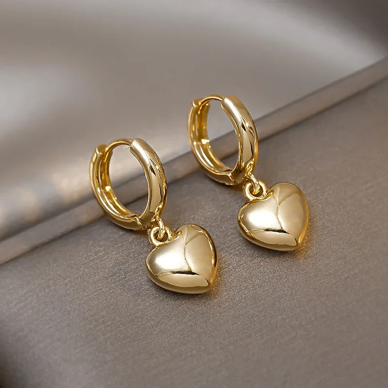 Elegant gold hoop earrings with dangling puffed heart charms, luxury fashion jewellery displayed on grey satin surface