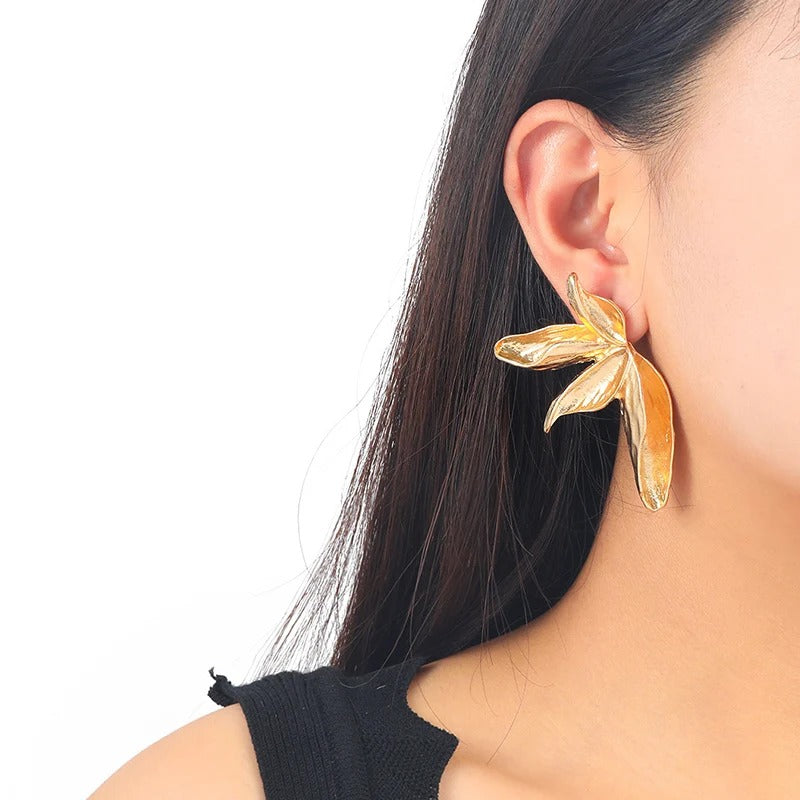 Gold leaf-shaped earring worn by a person with a plain background