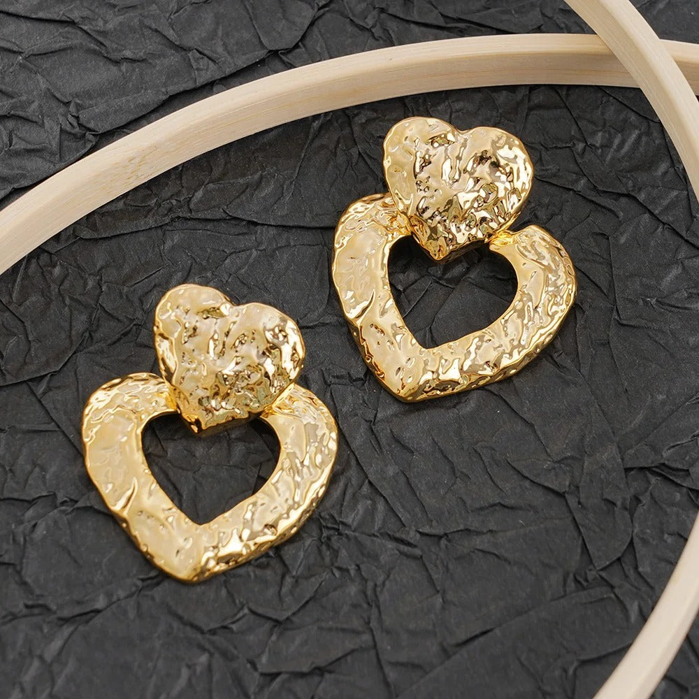 Gold heart-shaped earrings on a textured black surface