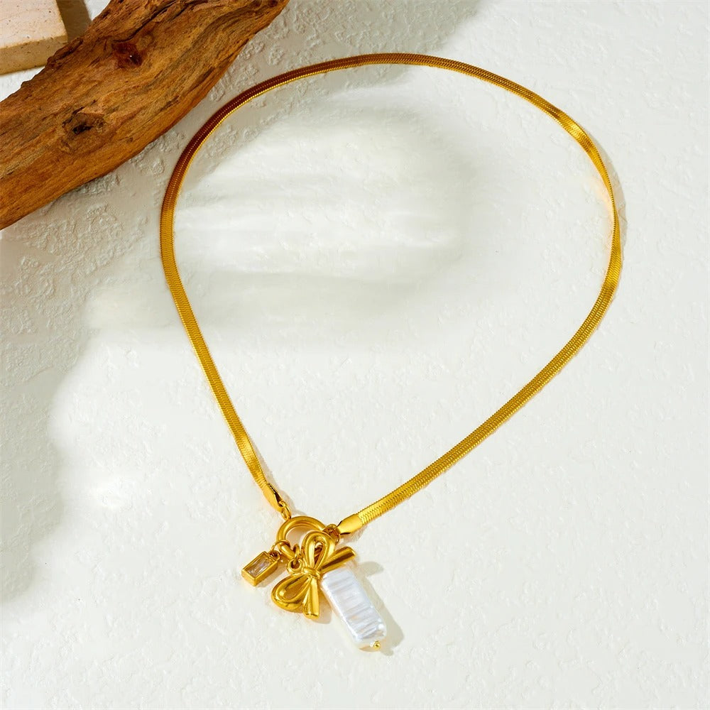 Gold necklace with a bow and heart charm on a light background