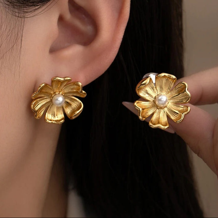 Gold flower-shaped earrings with a pearl center worn by a person.