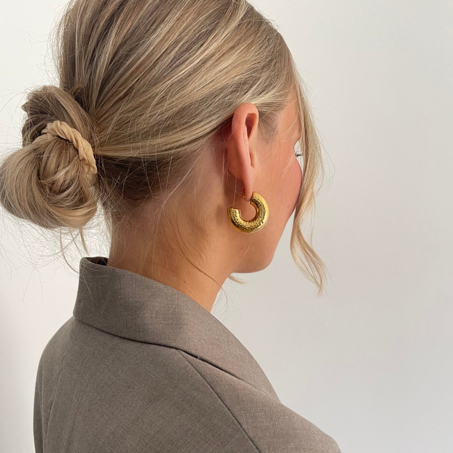Woman wearing gold hoop earrings with a neutral background