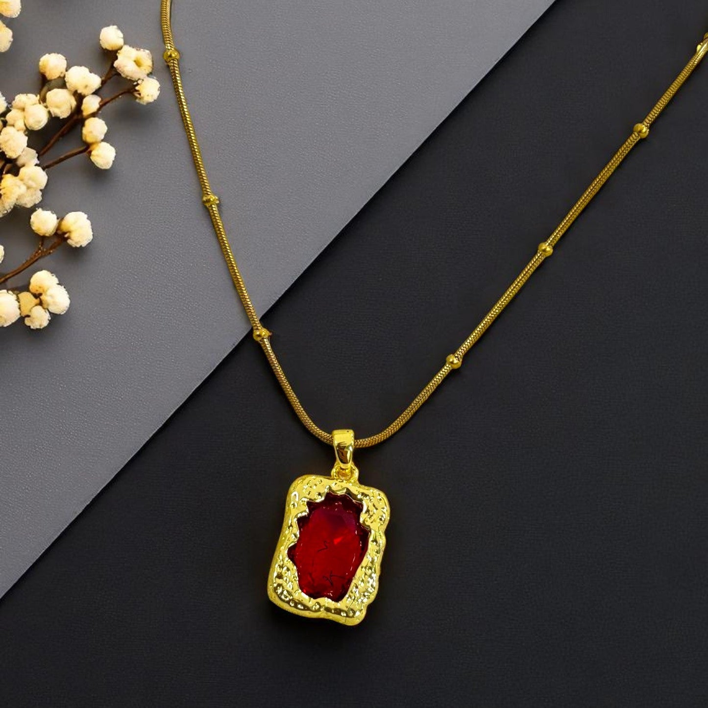 Elegant gold plated necklace with red stone pendant on dark background – Glampouch jewelry