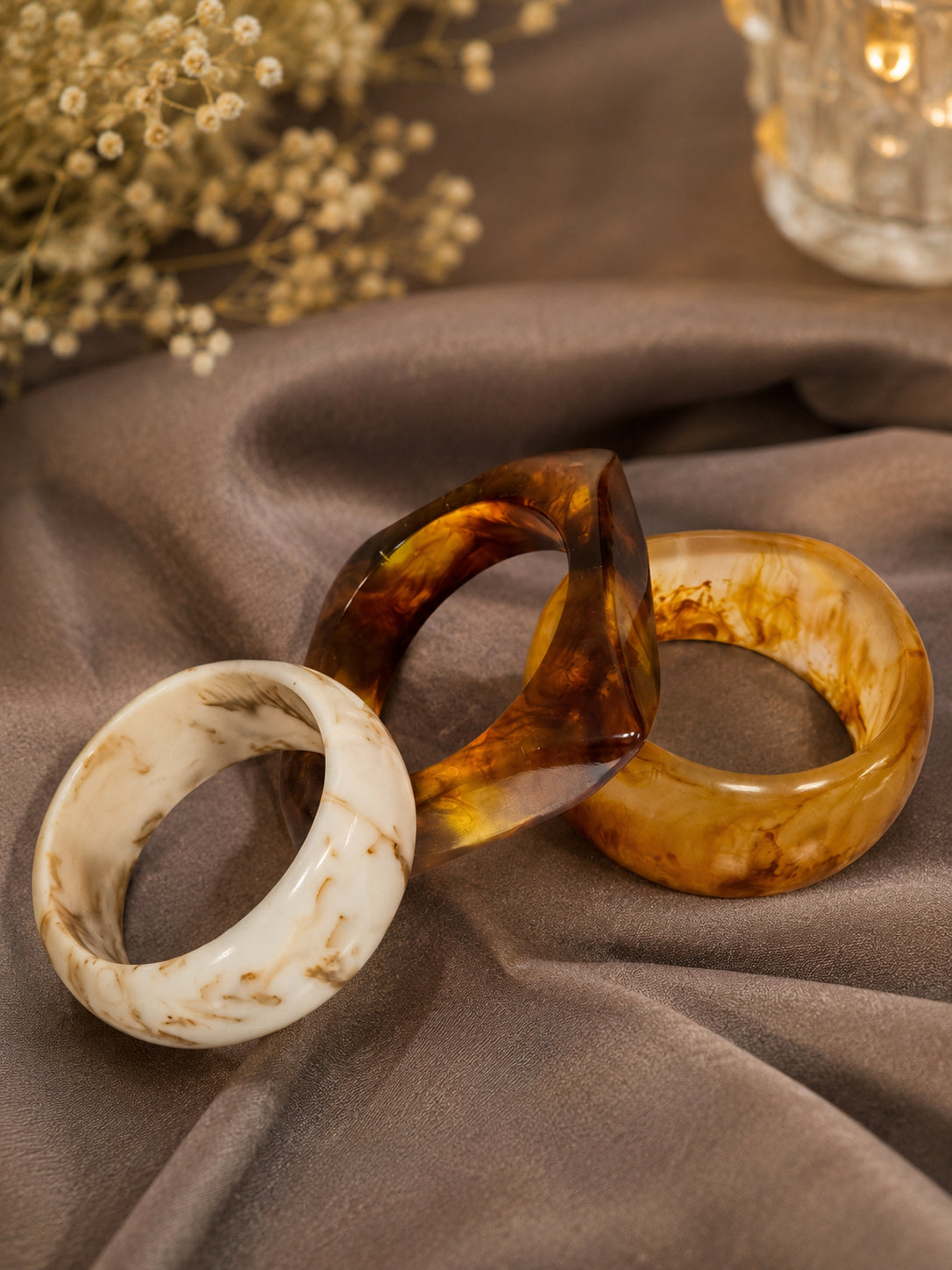 Three resin marble bangles in ivory, tortoiseshell, and amber arranged on grey satin with baby's breath flowers