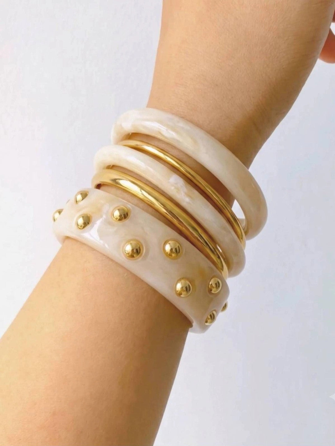Side view of the complete bangle stack on a wrist highlighting the layered ivory resin and gold-plated metal bangles