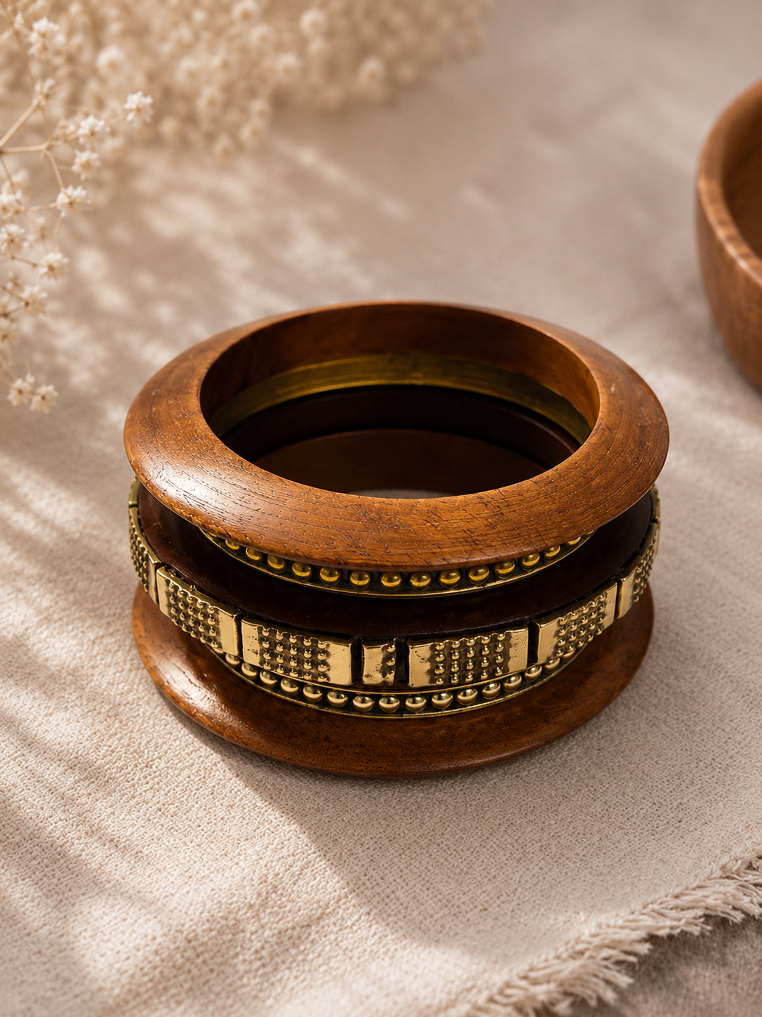 Four bangles stacked together on a textured beige cloth showing antique brass dot and block detailing clearly