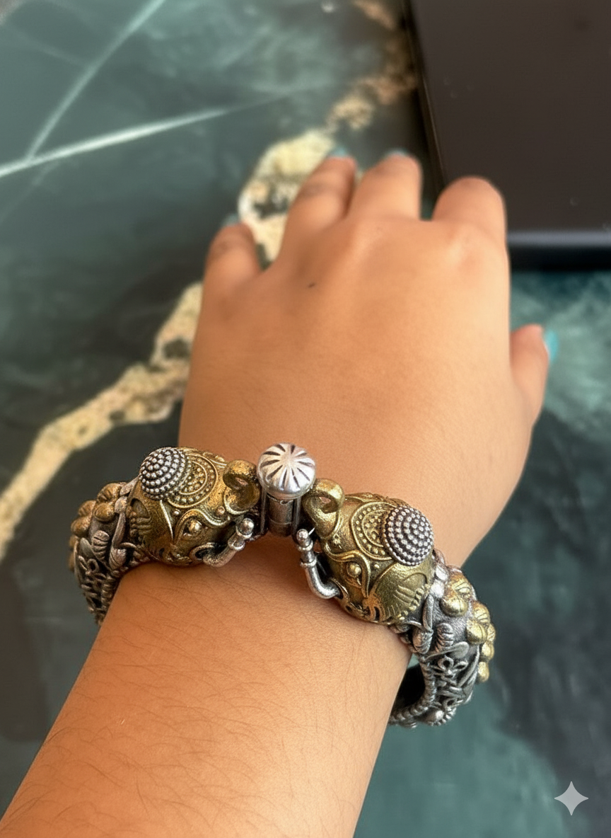 Hand wearing two ornate bracelets on a reflective surface