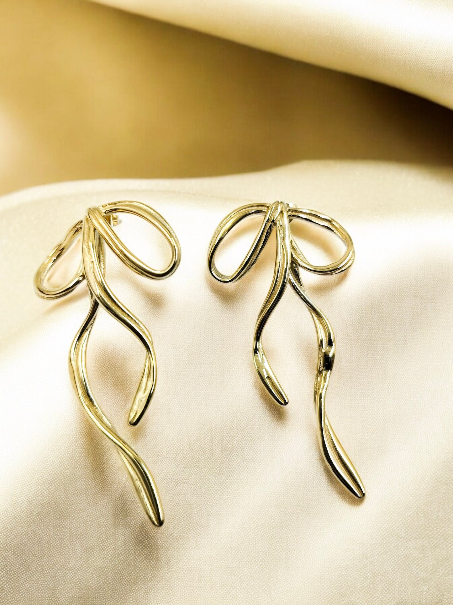A pair of gold-toned ribbon-shaped earrings laid on a white fabric surface.