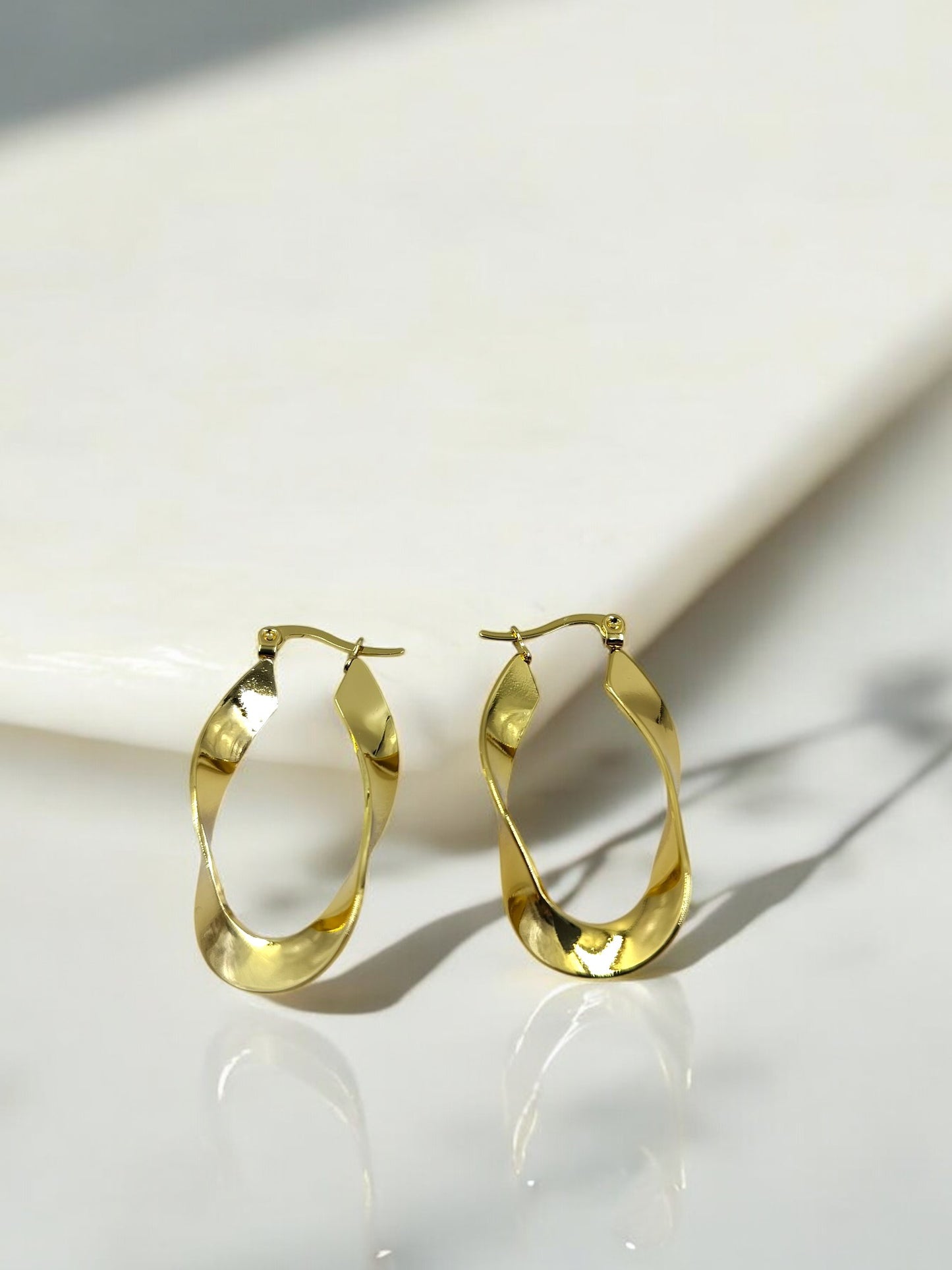 Chic twisted gold hoop earrings placed on a glossy marble surface, perfect lightweight jewelry for everyday modern style.