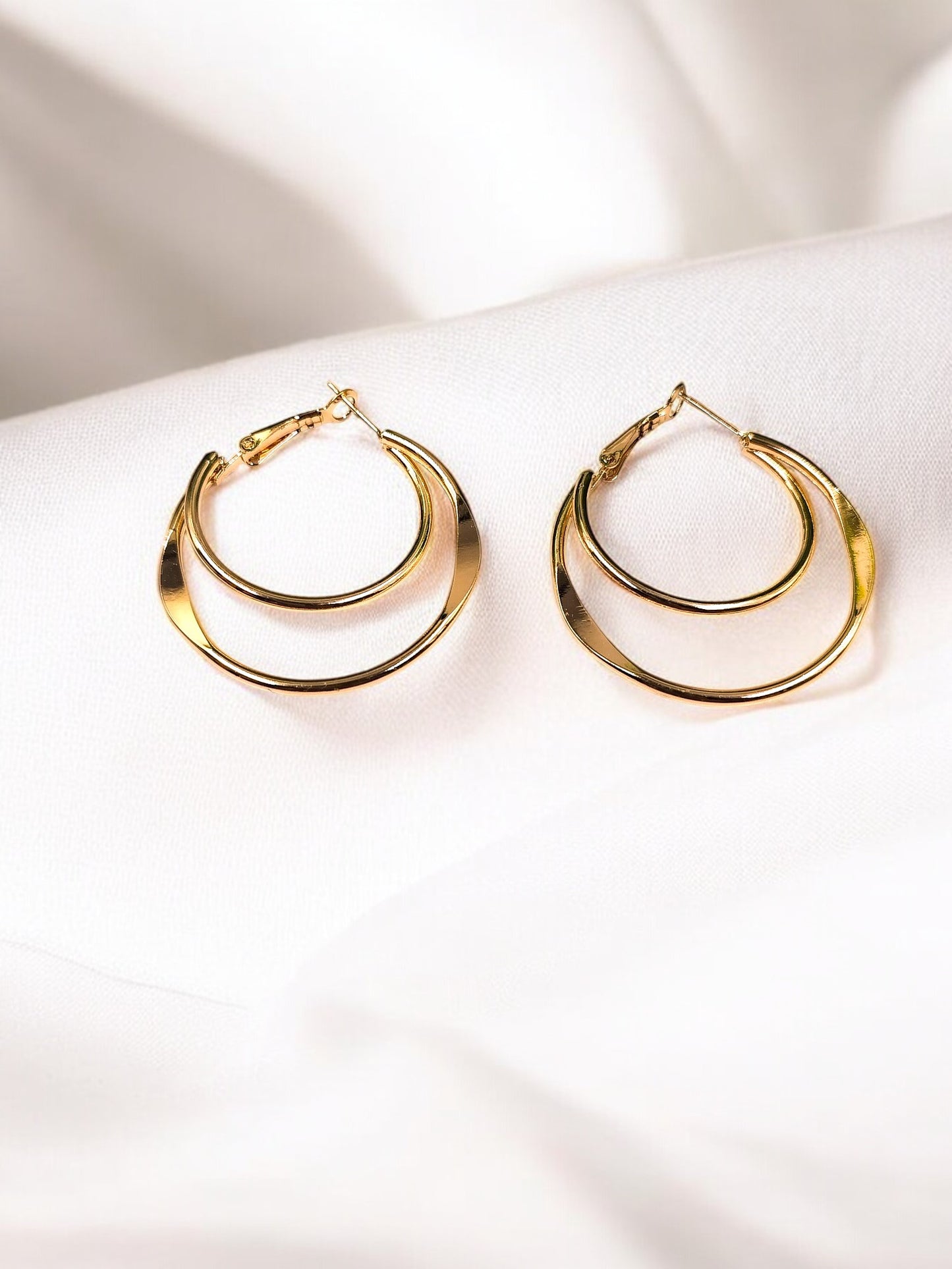 A pair of gold-toned hoop earrings with a textured surface, displayed on a white fabric background.