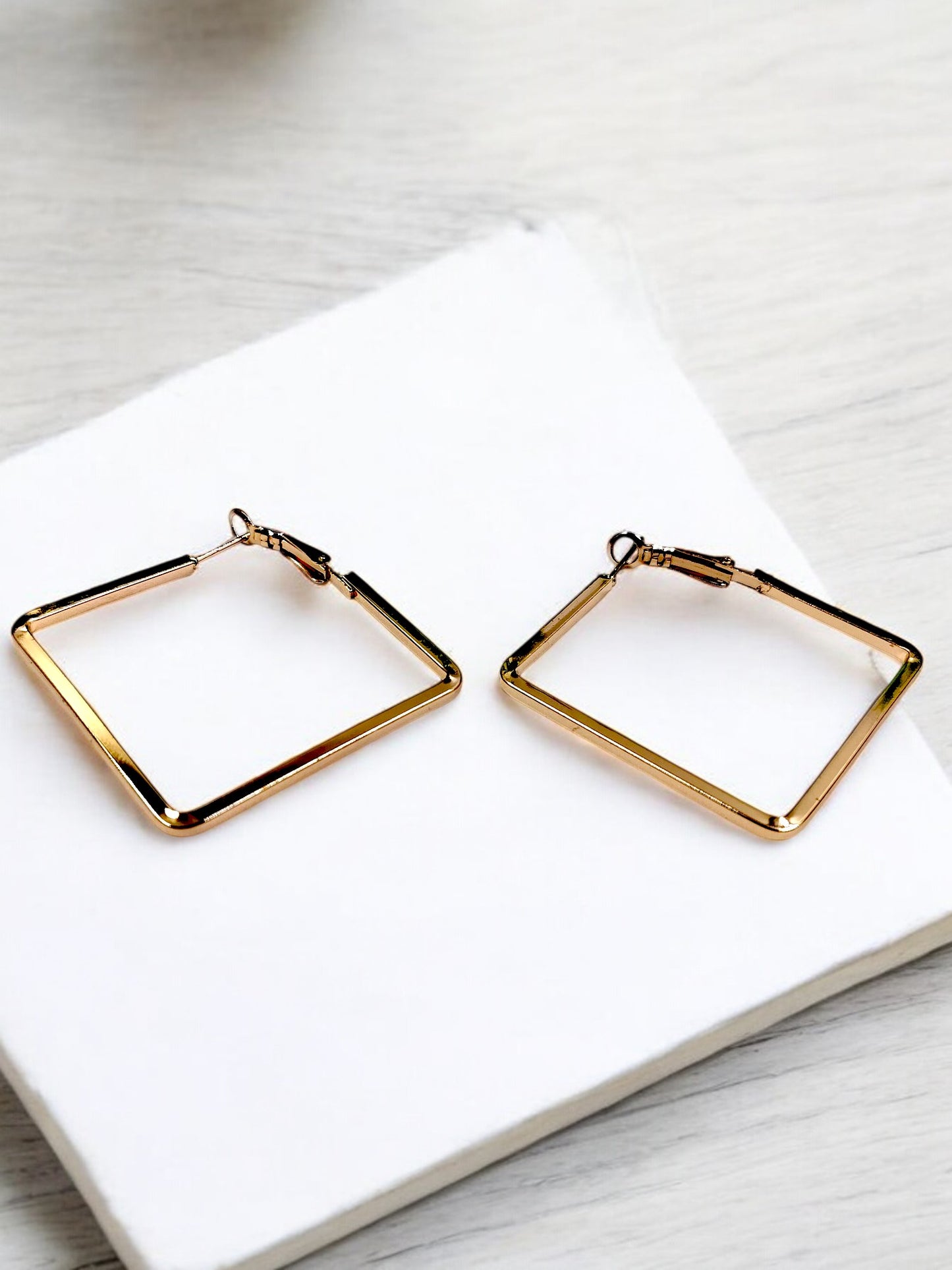 A pair of gold-tone hoop earrings with a squircle shape on a white surface.