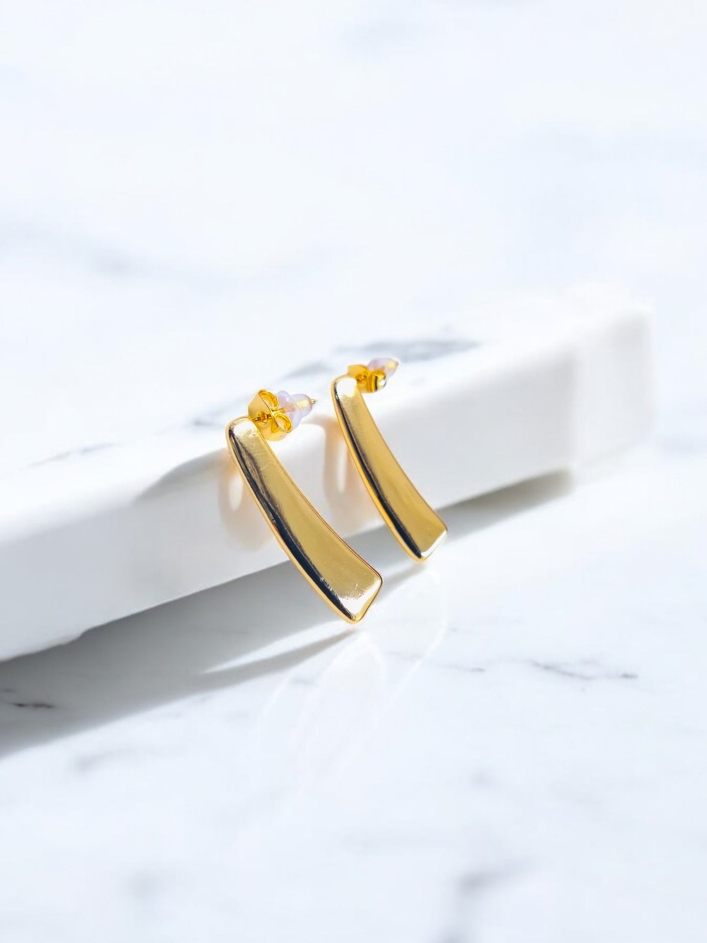 Minimalist gold bar stud earrings with a sleek modern design, displayed on a white marble surface.