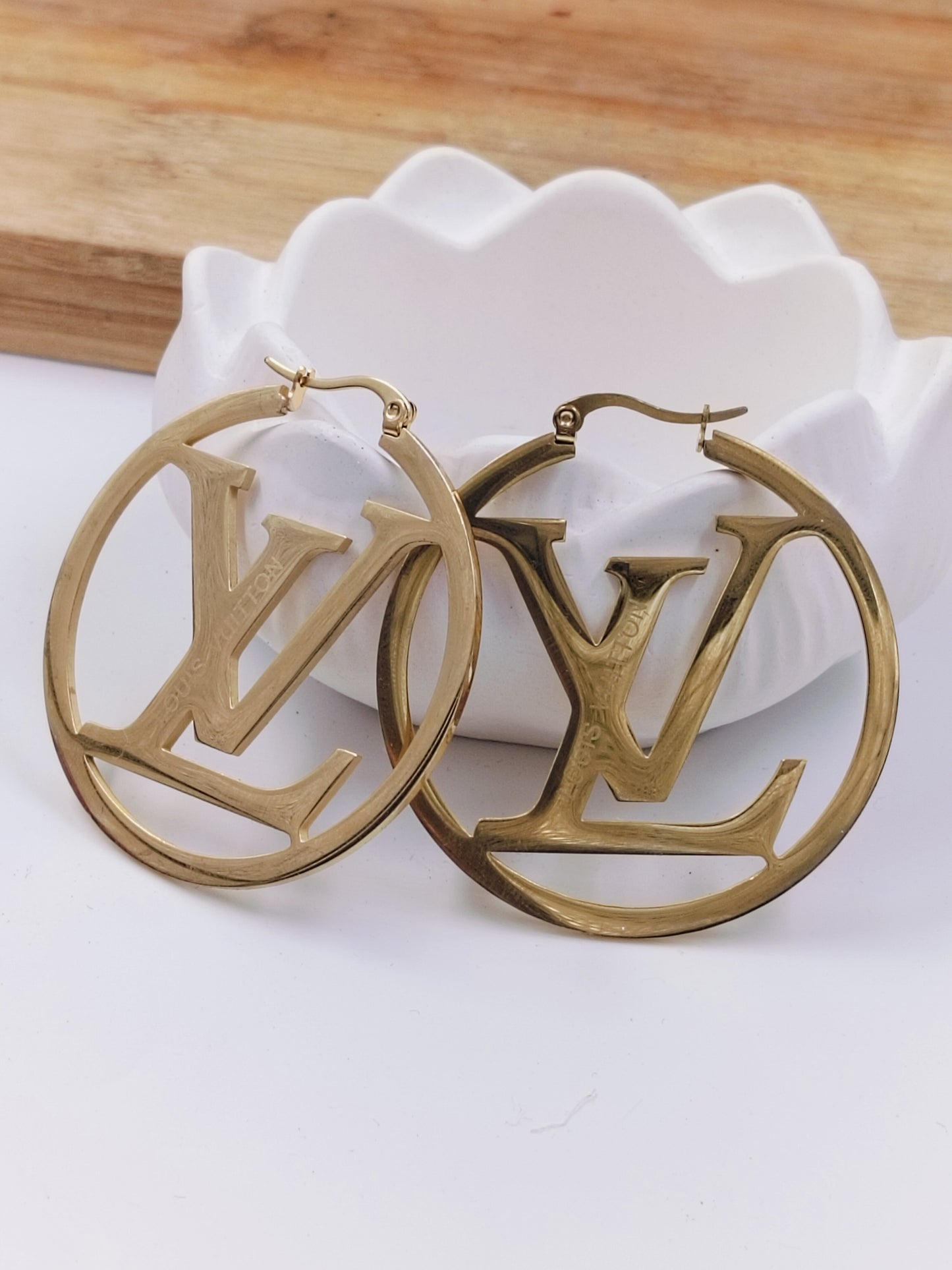 A pair of gold-plated hoop earrings with a signature monogram design, displayed on a white surface.