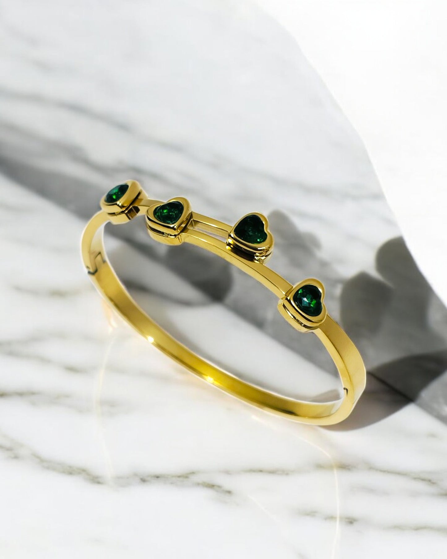 Elegant gold plated bangle adorned with four green heart-shaped stones, a timeless jewelry piece perfect for parties, gifting, and everyday sophistication.