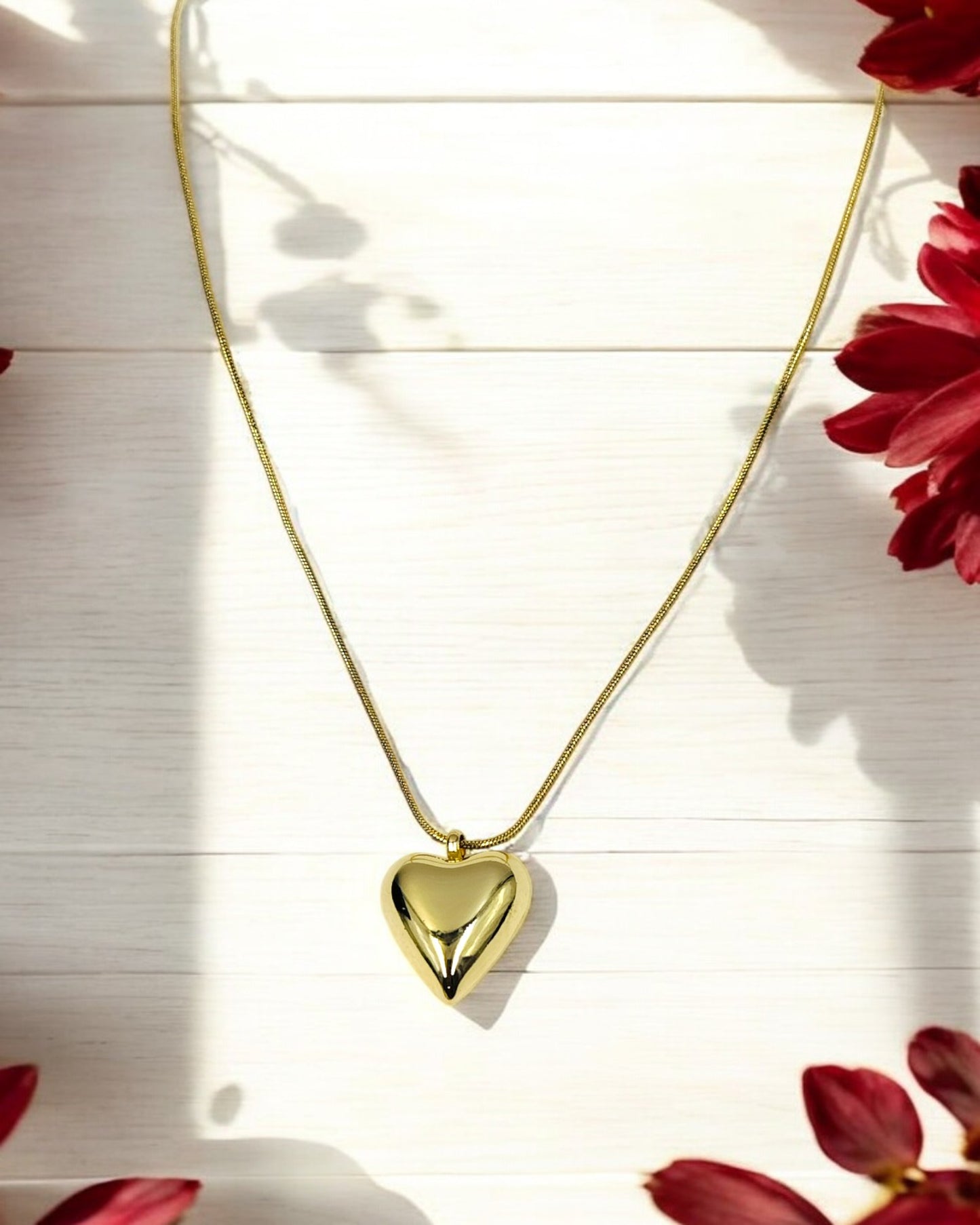 A gold-colored heart pendant chain necklace laid out on a flat surface with a floral pattern in the background.