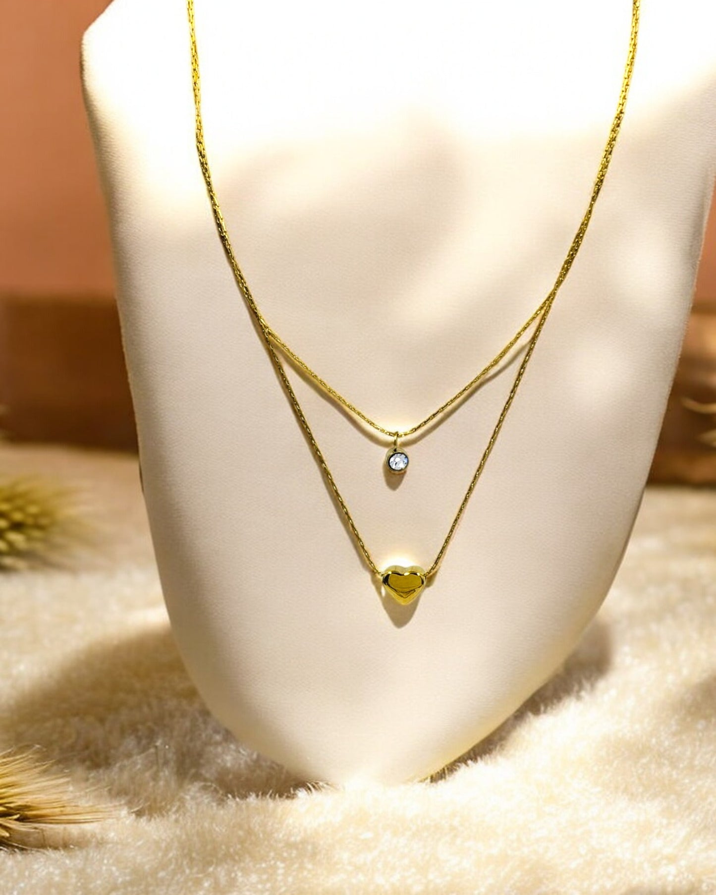 Gold layered necklace with heart pendant and solitaire crystal charm on display stand, elegant women’s jewelry