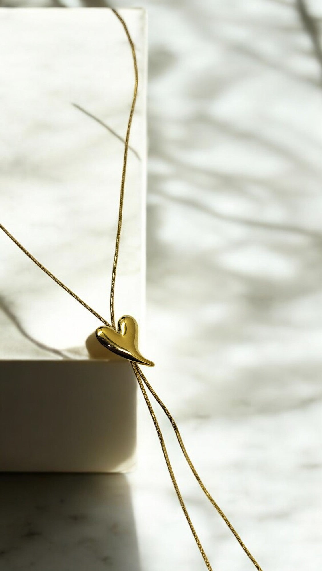 A gold Y-shaped necklace with a sculpted heart accent and diamond tips, displayed against a neutral background.