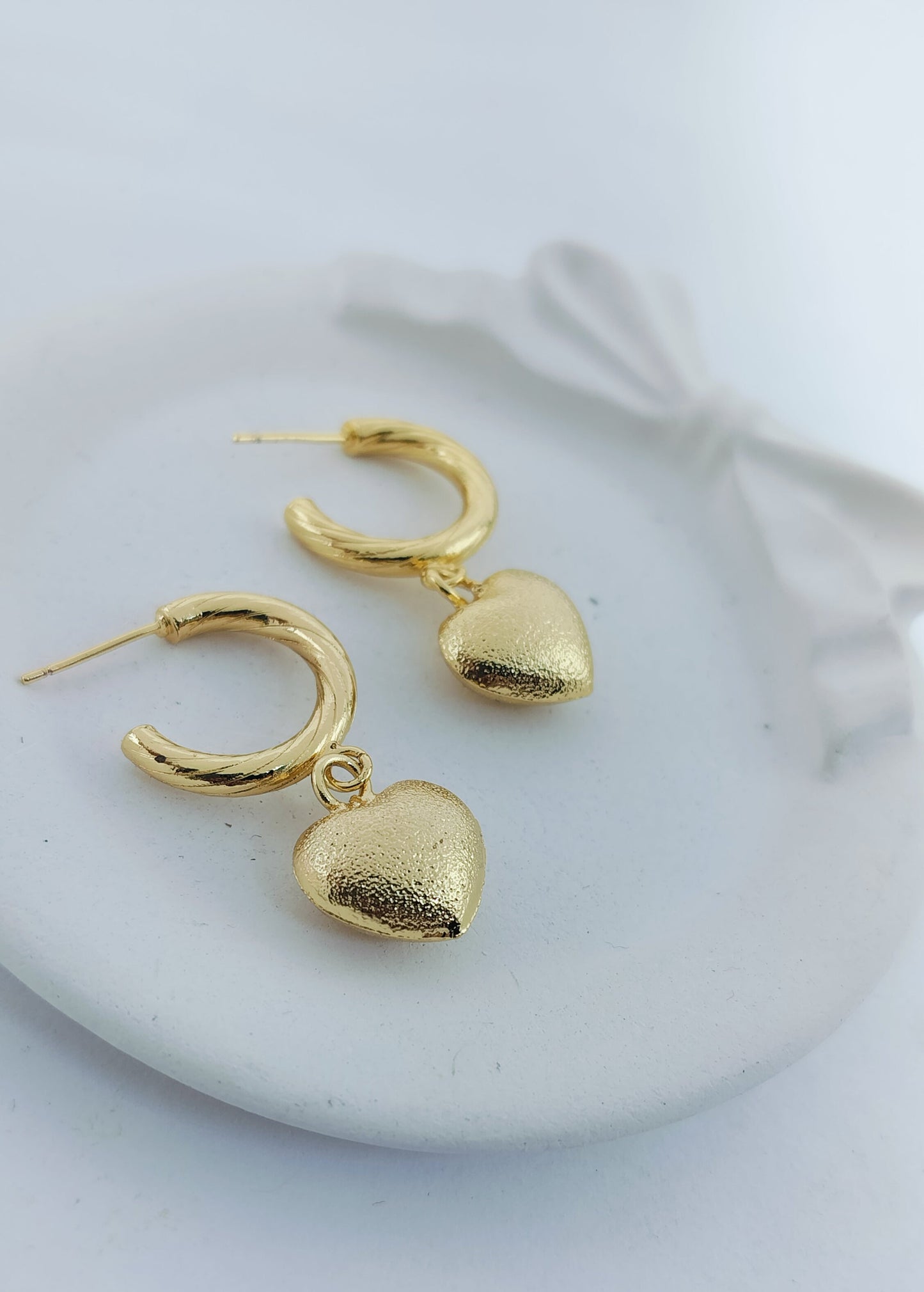 Elegant gold hoop earrings with dangling textured heart charms, perfect for romantic and everyday jewelry looks.