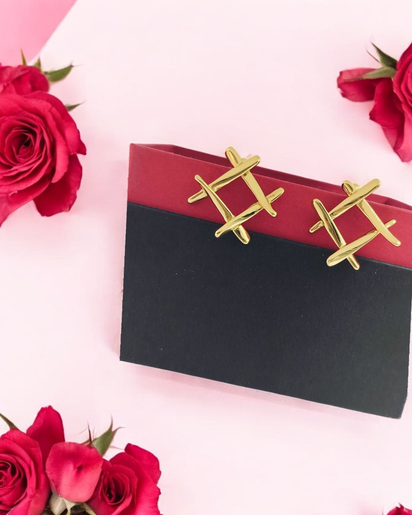 Trendy gold geometric stud earrings with crisscross design, displayed on gift box with red roses for stylish look.