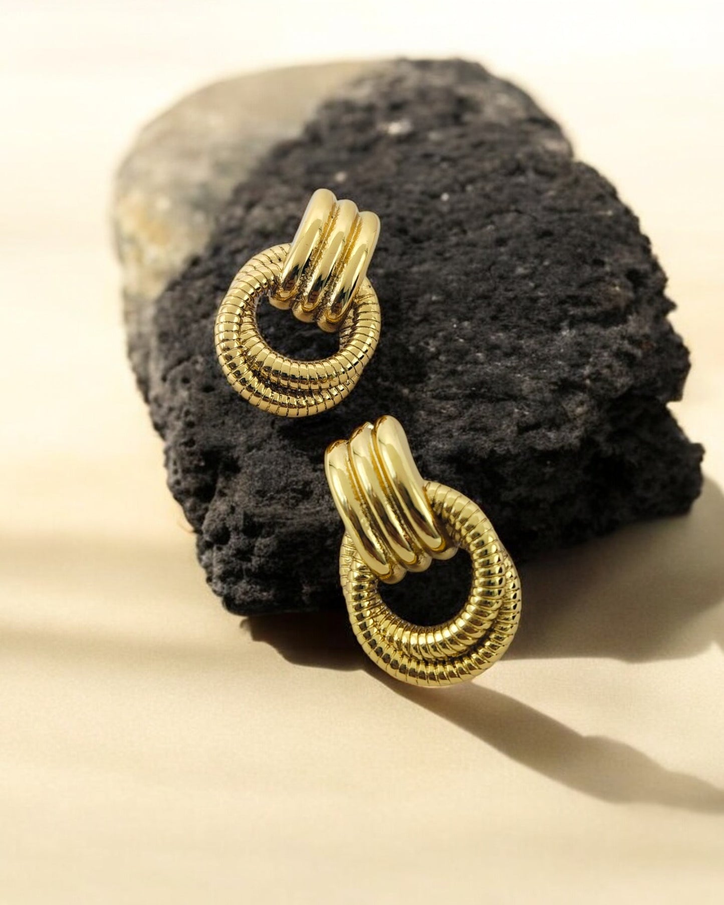 Textured gold loop earrings with layered circular design placed on a black stone, elegant statement jewellery piece