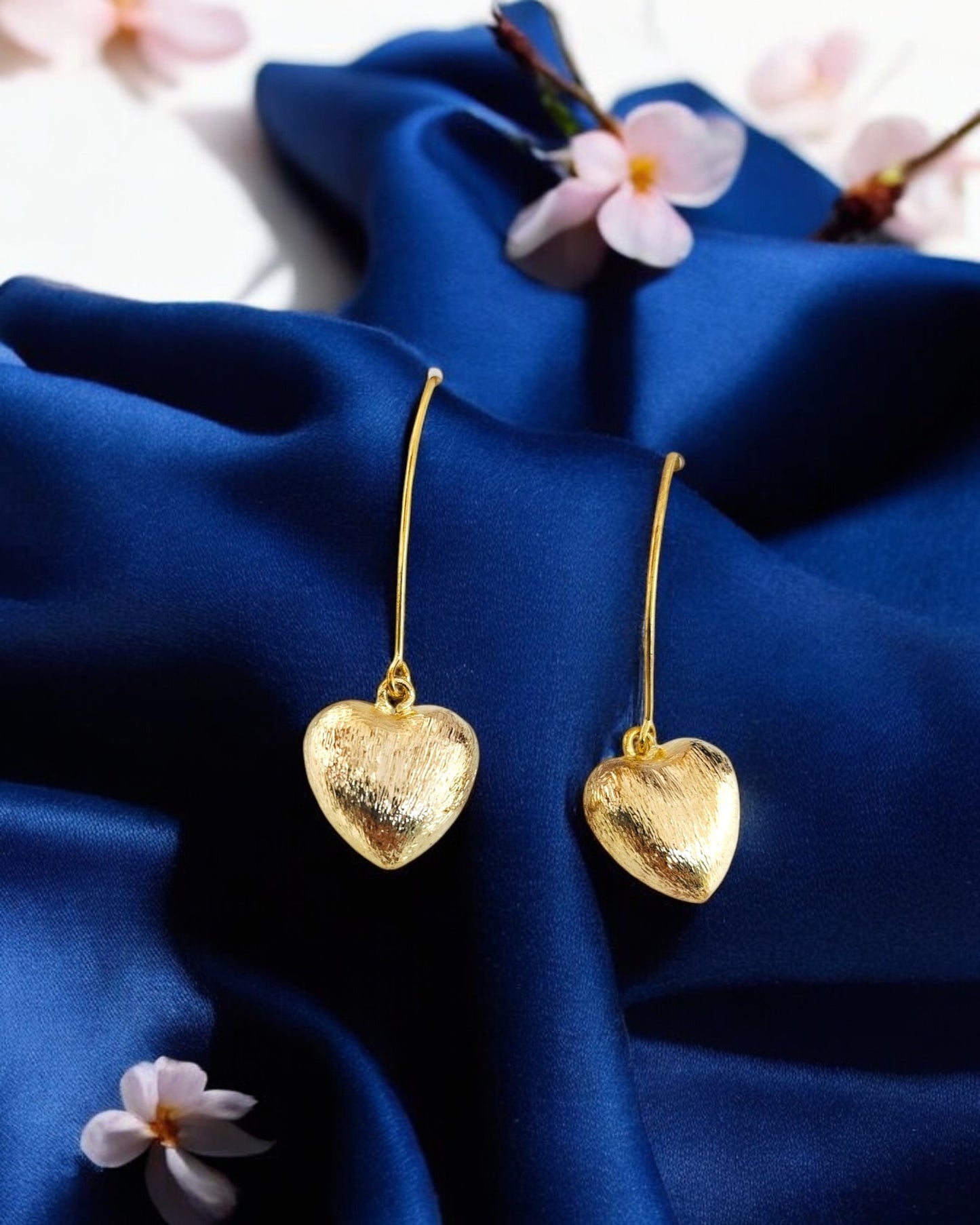 Golden heart shape earrings on blue silk background, elegant fashion jewellery perfect for women style & gifting.