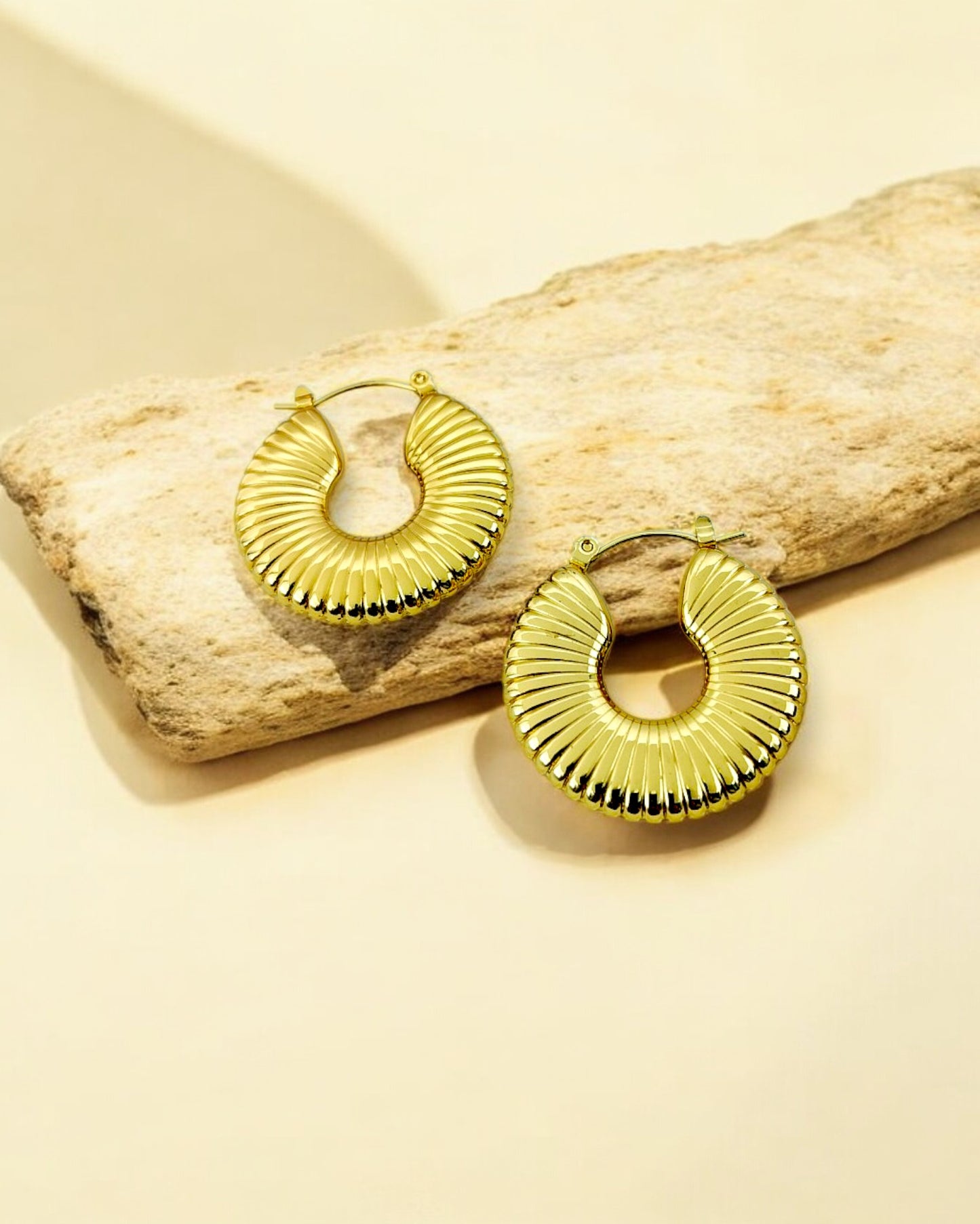 A pair of gold-plated ribbed coil hoop earrings resting on a beige surface.