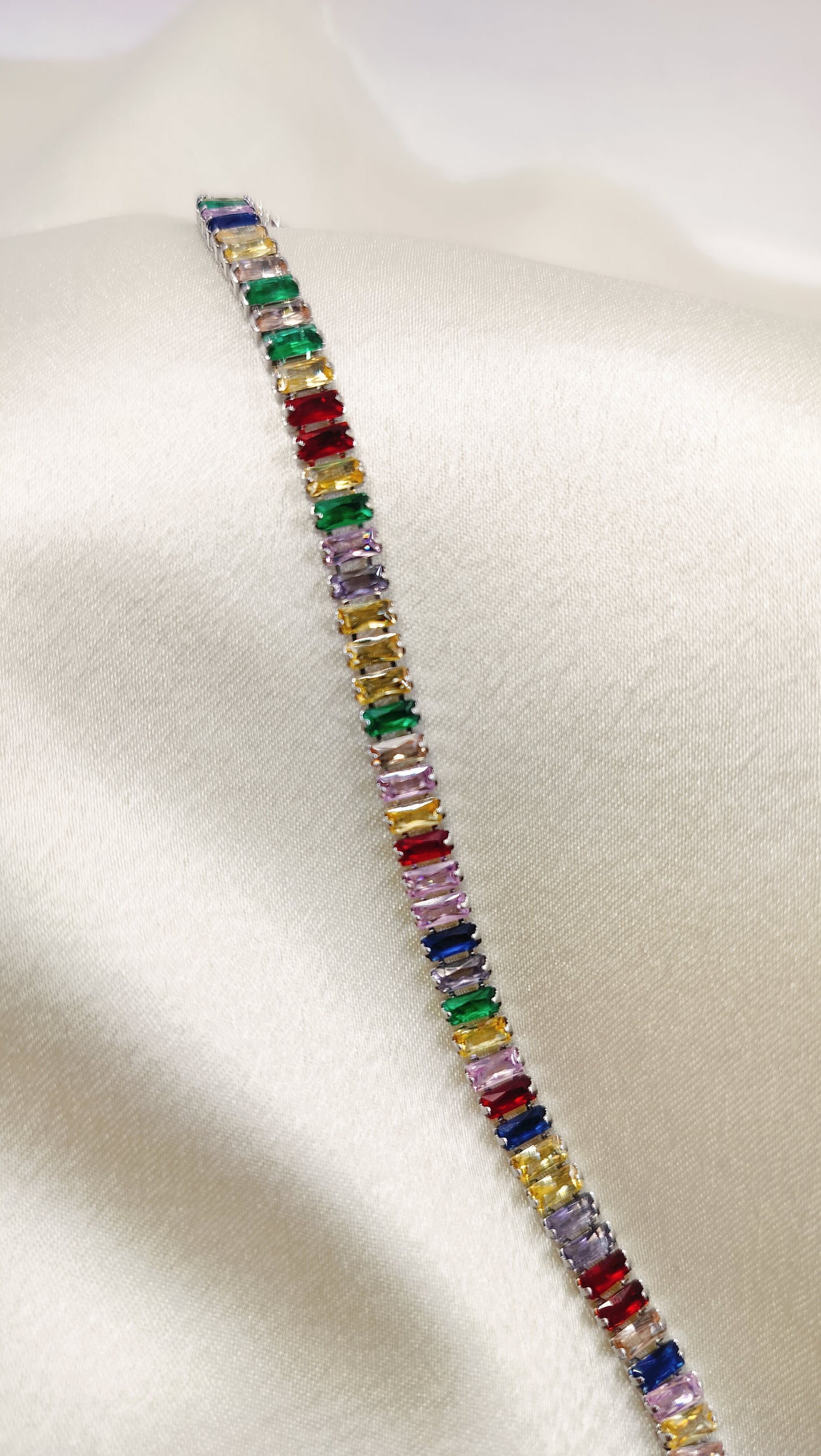Silver or white gold tennis bracelet with multicolored baguette-cut stones on a satin background.