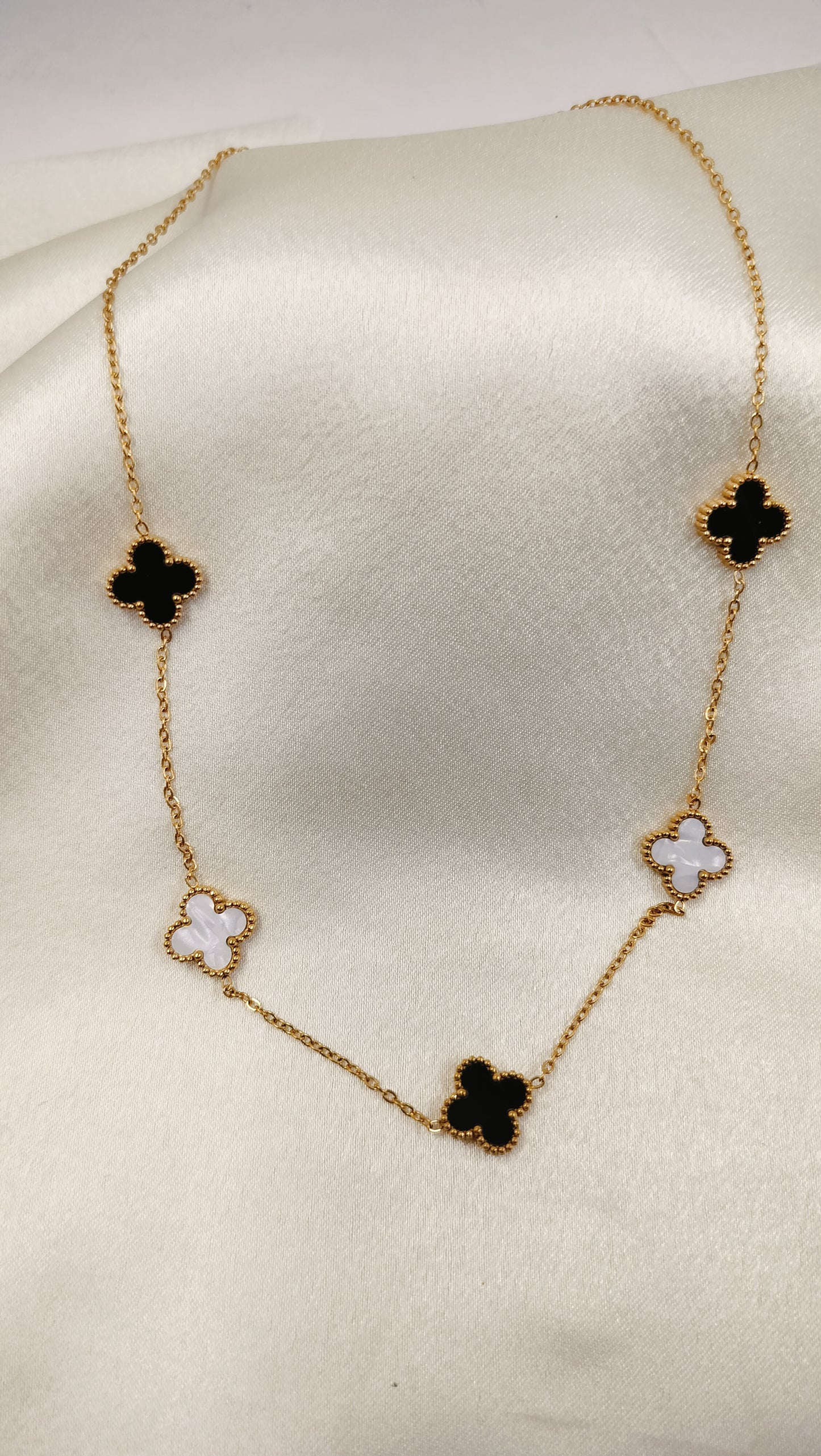 Gold chain necklace with black onyx and white mother-of-pearl clover motifs.