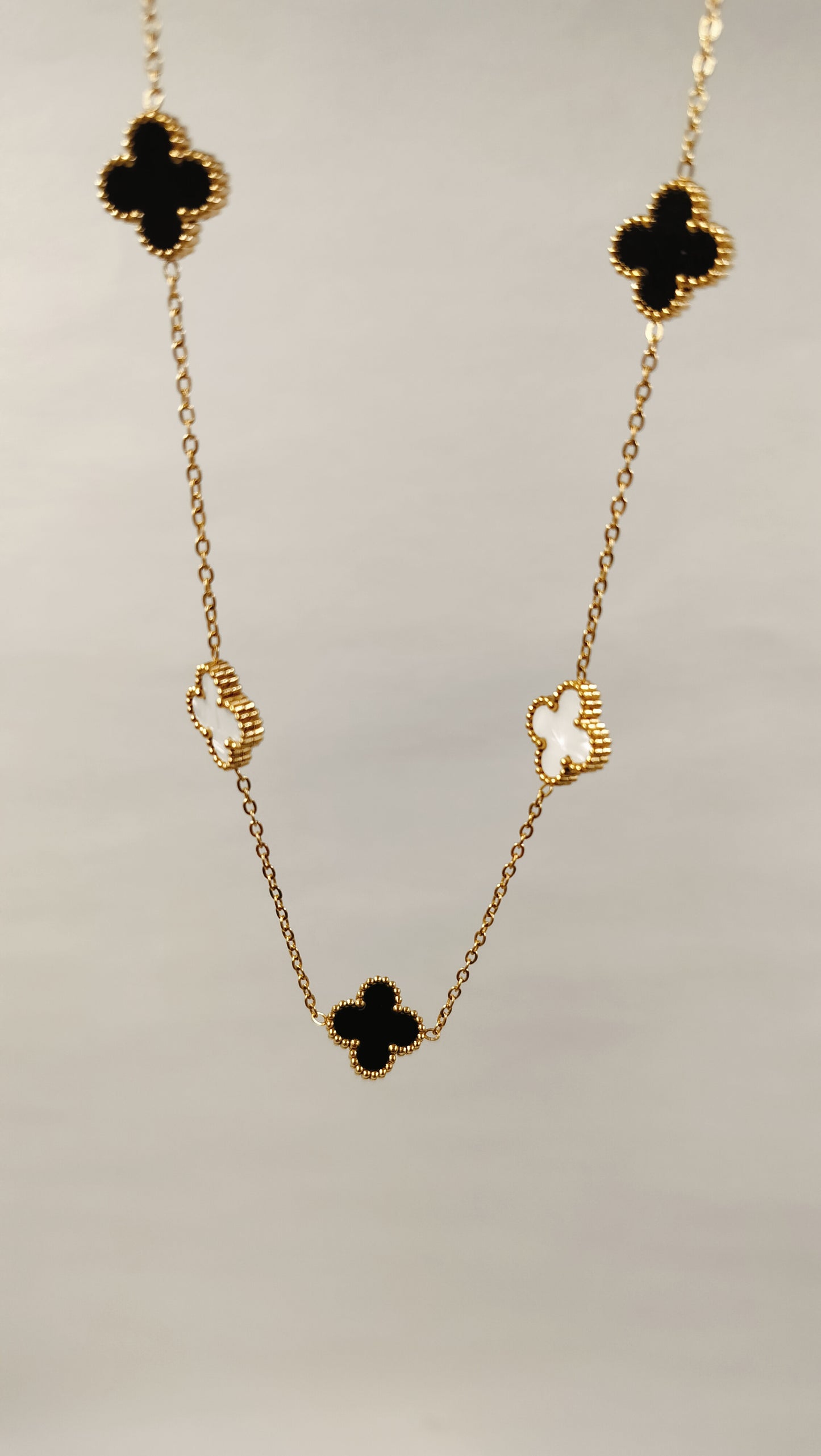 Gold chain necklace with black onyx and white mother-of-pearl clover motifs.