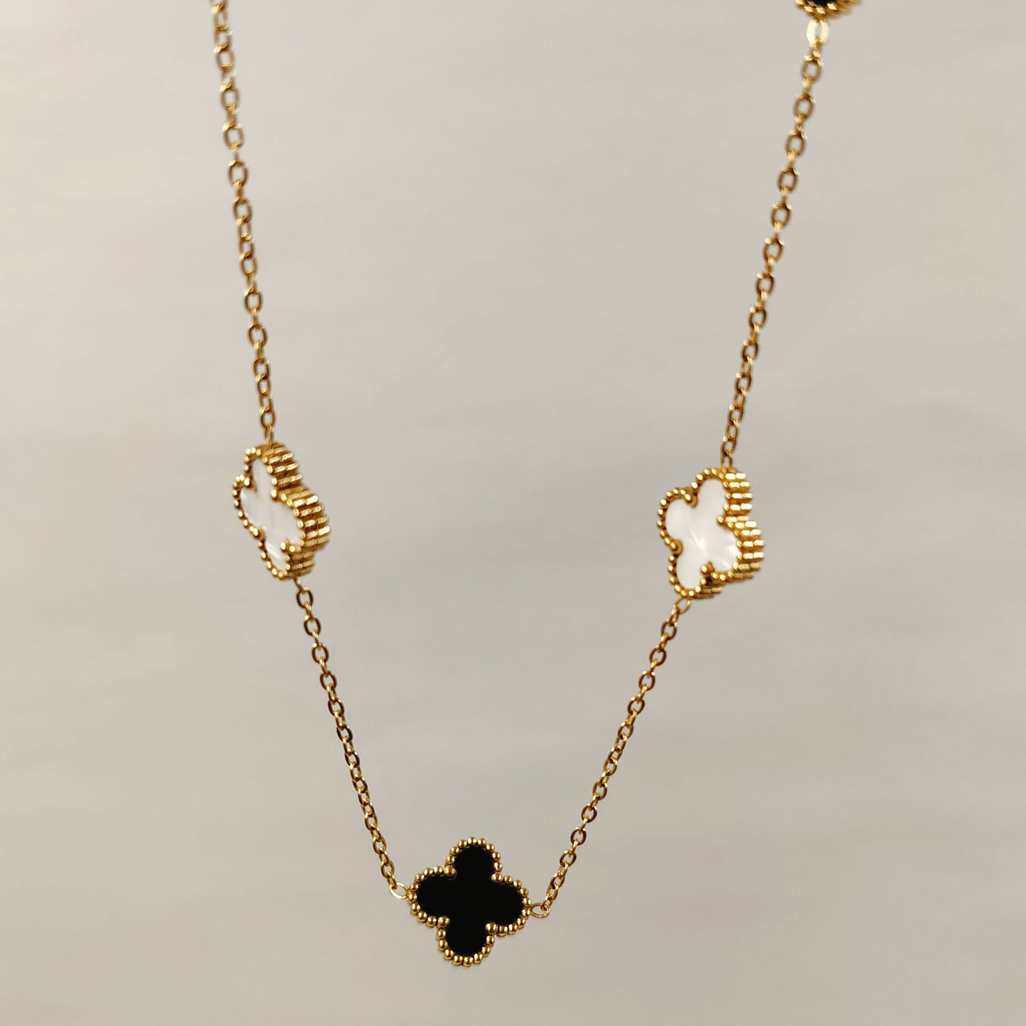 Gold chain necklace with black onyx and white mother-of-pearl clover motifs.