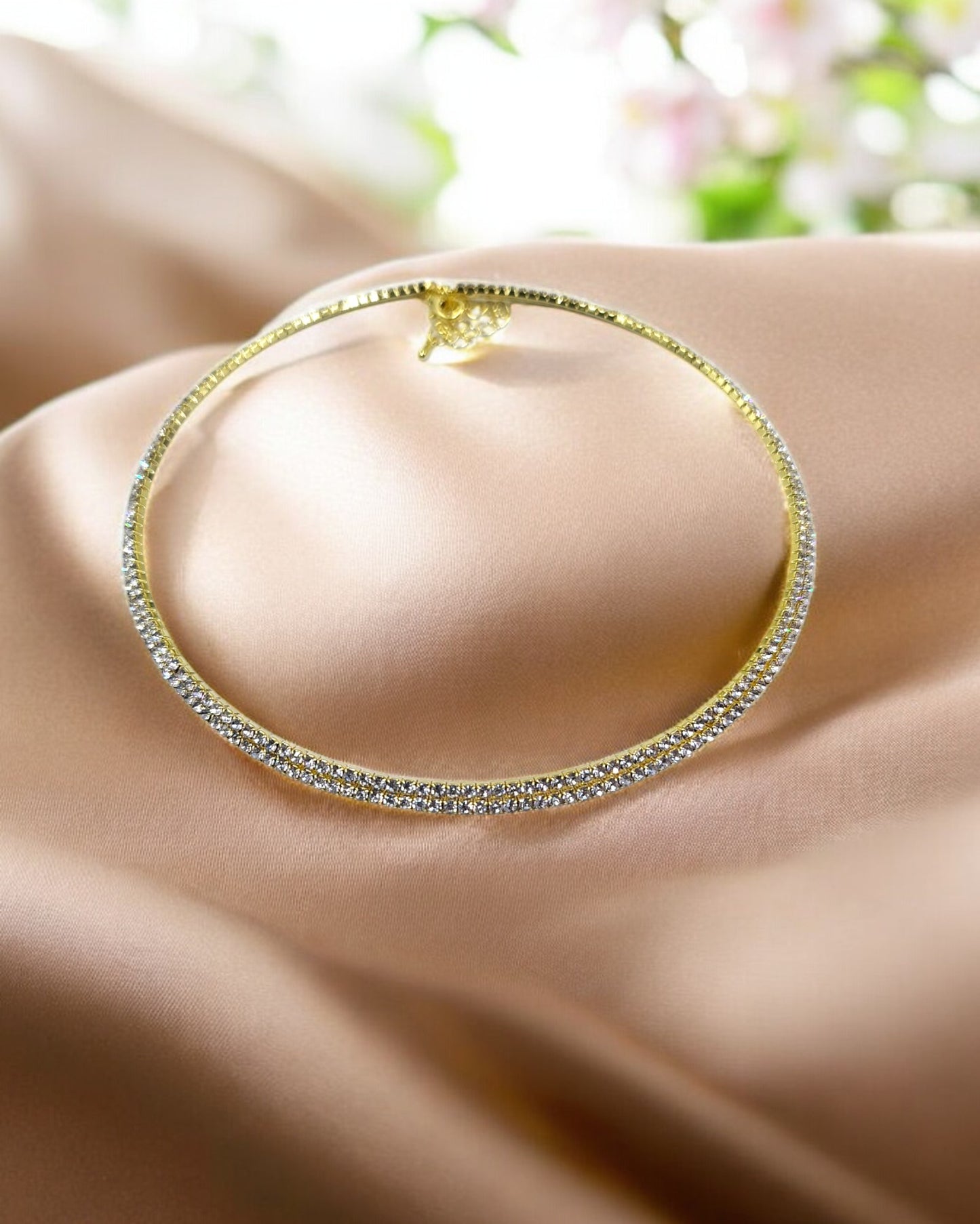 A gold-tone choker necklace encrusted with a row of dazzling crystals, displayed on a fabric surface.