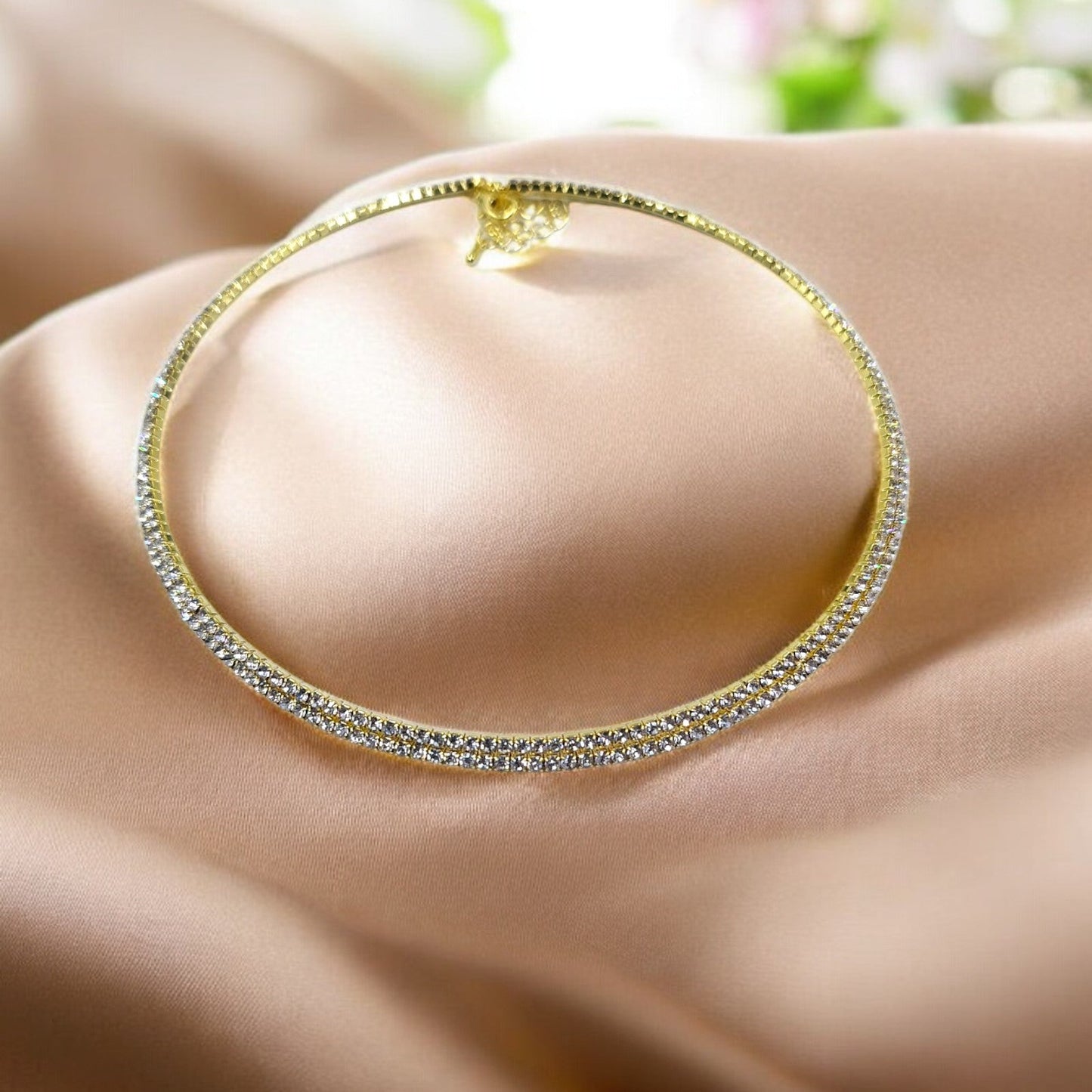 A gold-tone choker necklace encrusted with a row of dazzling crystals, displayed on a fabric surface.