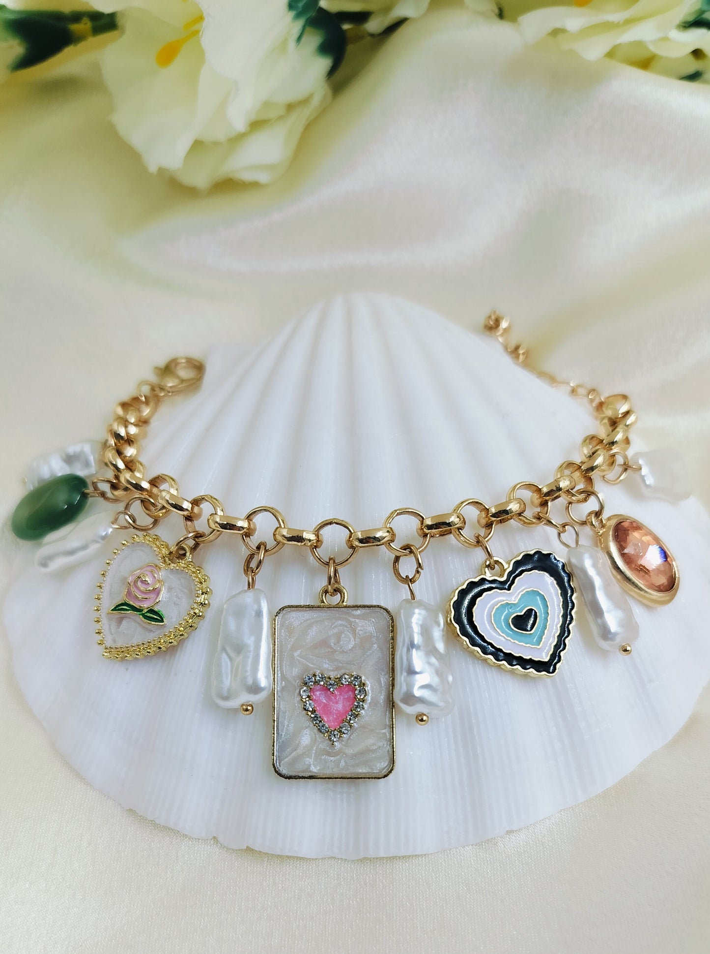 A gold-colored bracelet with various charms including a heart and floral design, displayed on a white surface.
