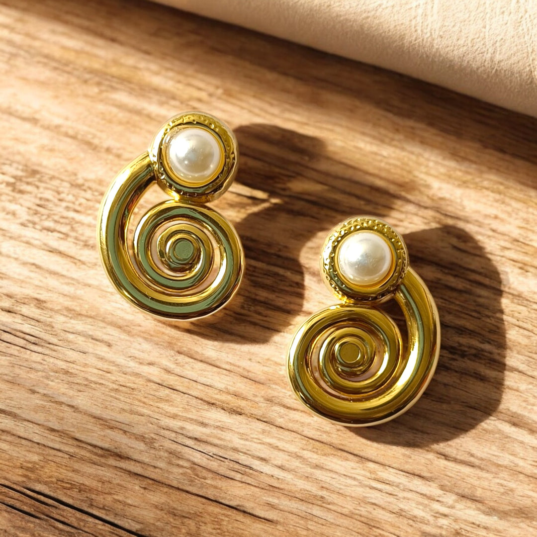 Gold earrings with pearl-like centers on a wooden surface
