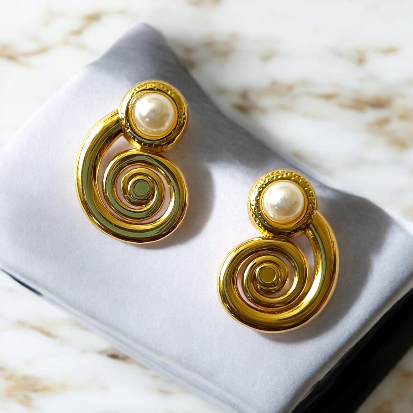 Gold spiral earrings with pearl accents on a gray cushion.