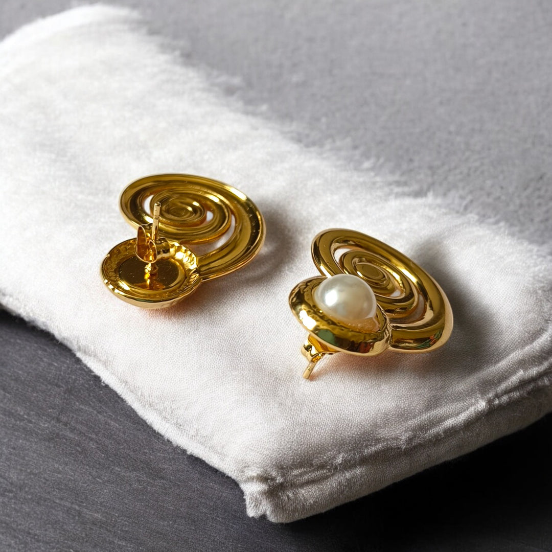 Gold spiral earrings with a pearl center on a white cloth