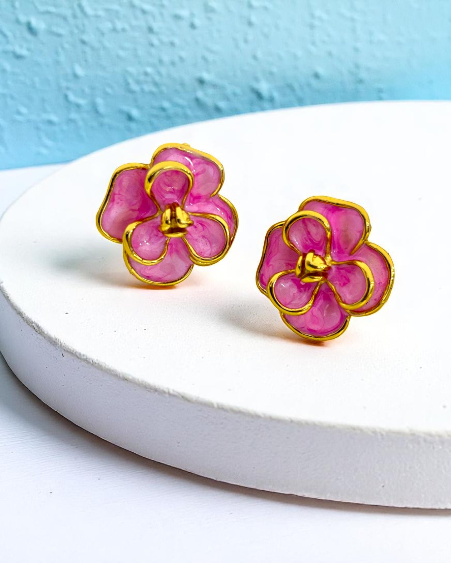 Gold plated floral stud earrings with pink enamel design displayed on white stand – Glampouch jewelry