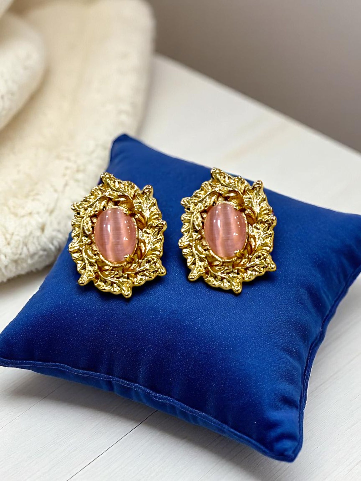 Gold plated stud earrings with oval pink gemstone displayed on blue velvet cushion – Glampouch jewelry