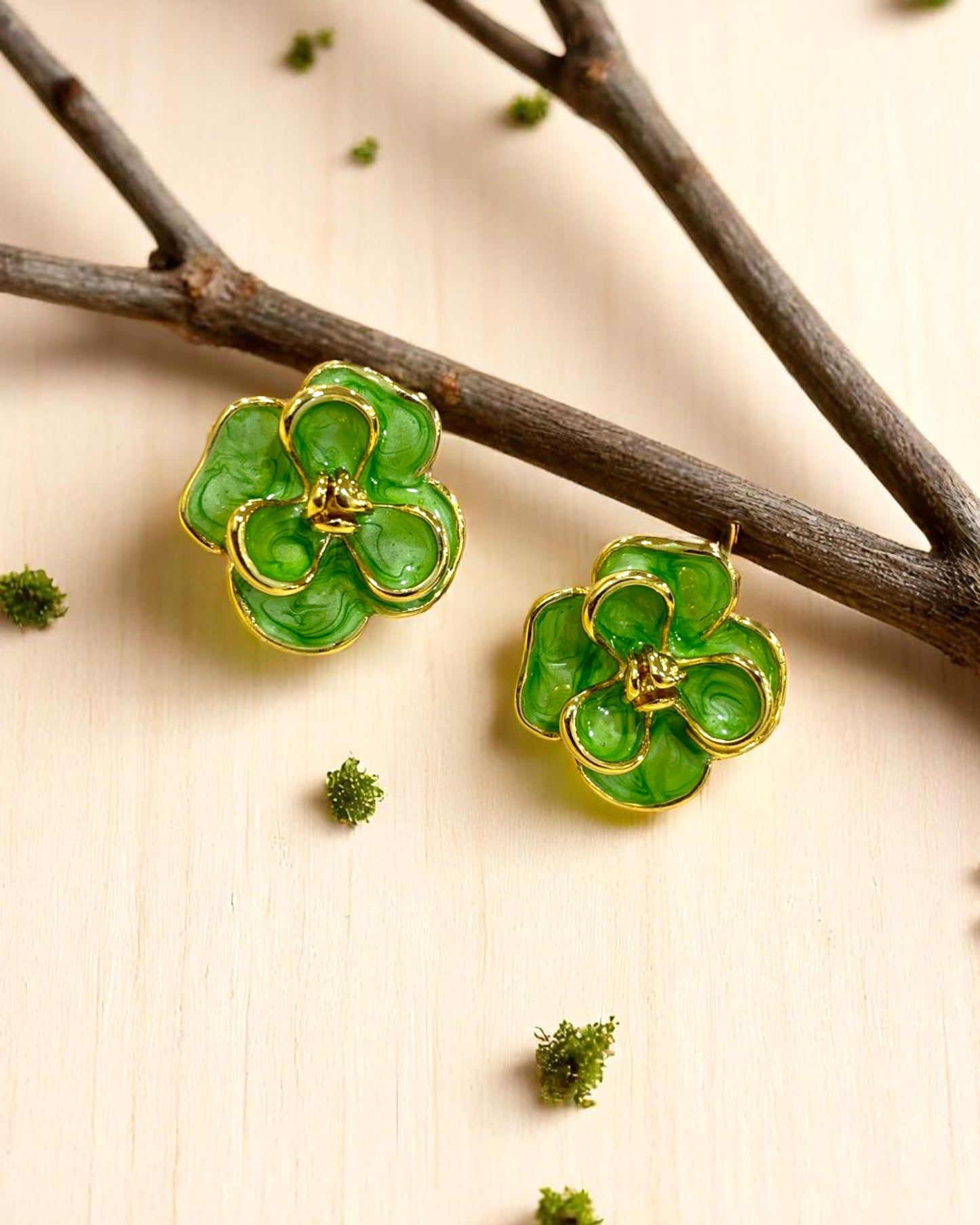 Elegant green enamel floral stud earrings with gold outlines, styled on a wooden surface with twigs β Glampouch jewelry