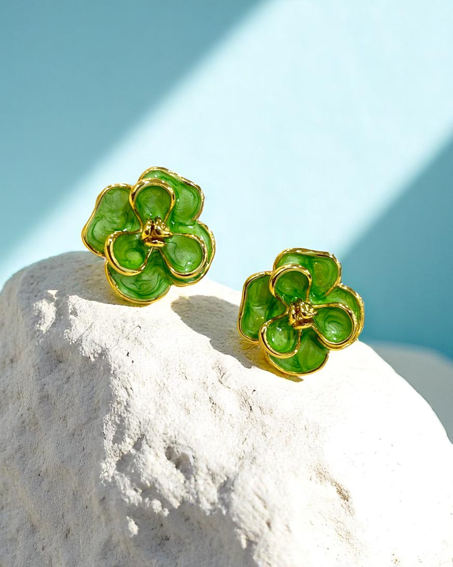 Gold plated floral stud earrings with glossy green enamel petals placed on a white stone β Glampouch jewelry