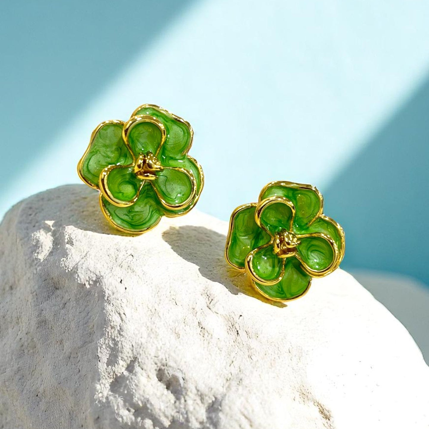 Gold plated floral stud earrings with glossy green enamel petals placed on a white stone β Glampouch jewelry