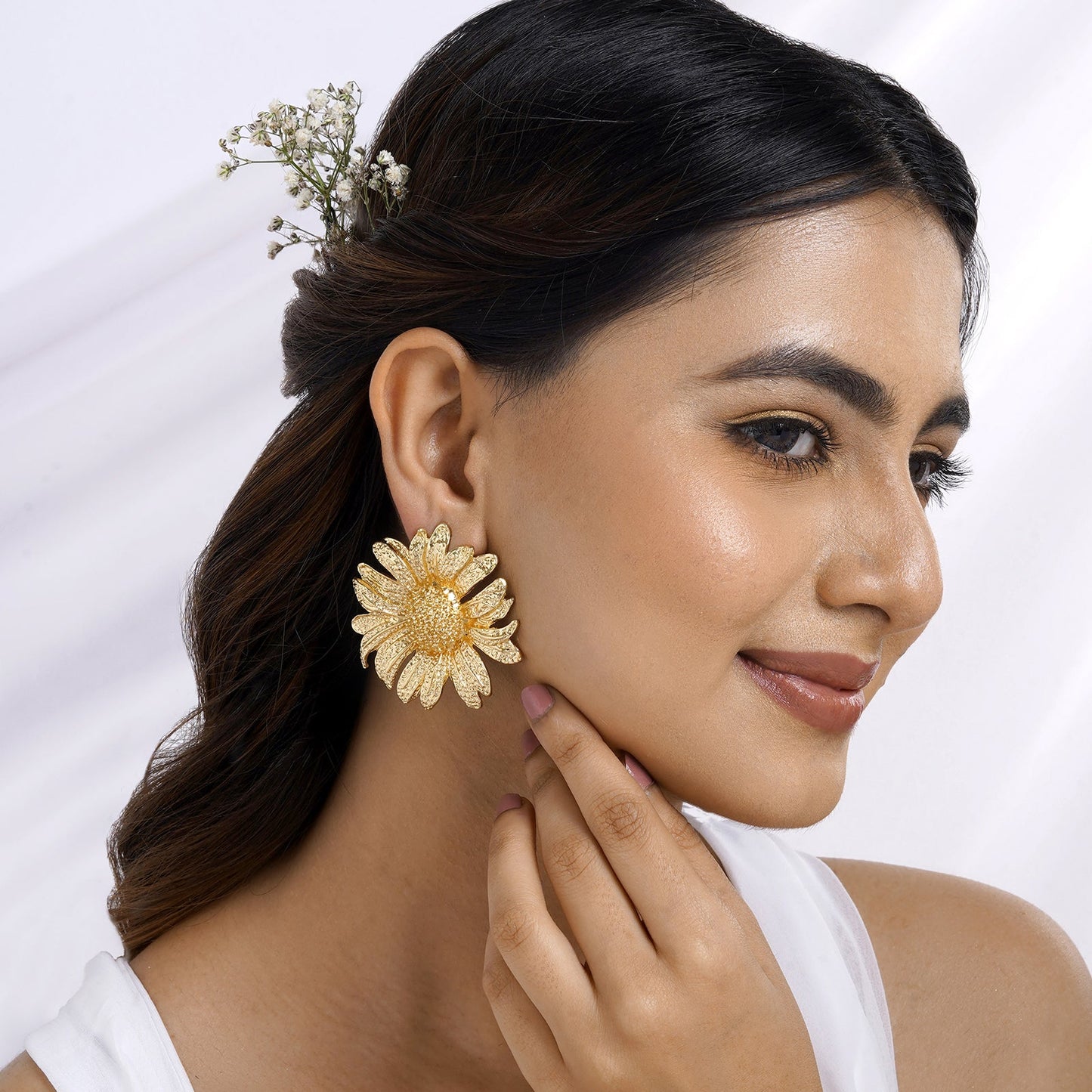 Beautiful woman wearing oversized floral gold statement earrings, styled with soft makeup and elegant hair adorned with delicate flowers – a perfect festive and bridal jewelry look.