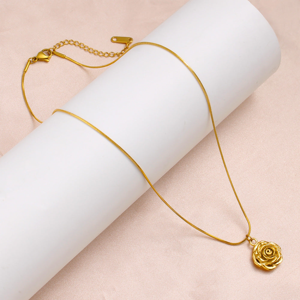 Gold necklace with a rose pendant on a white cylindrical object against a pink background