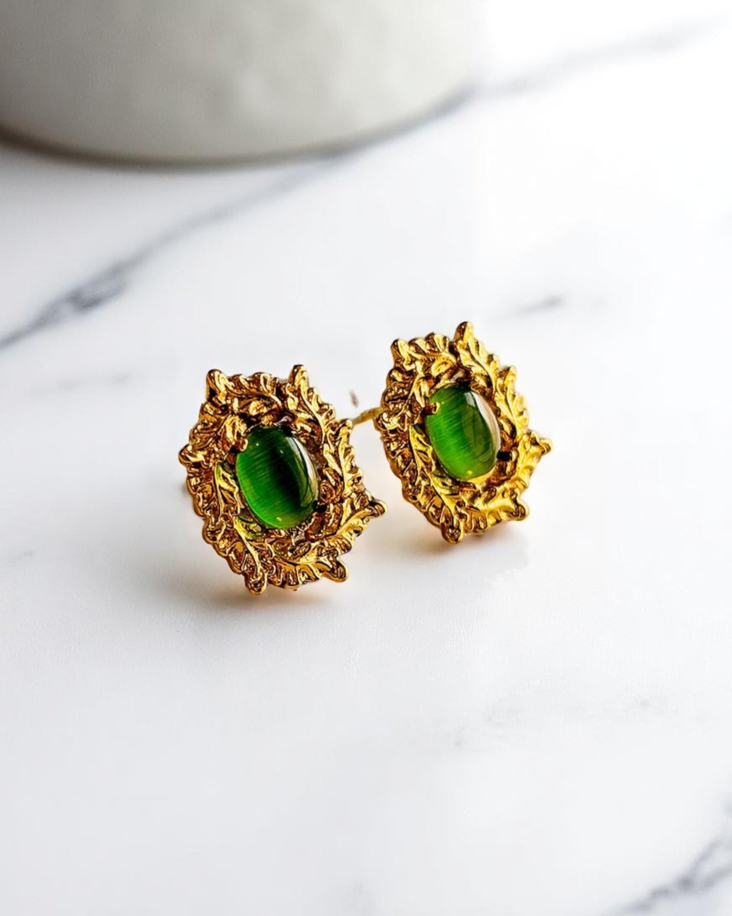 Elegant gold plated stud earrings with green gemstone on white marble surface – Glampouch jewelry