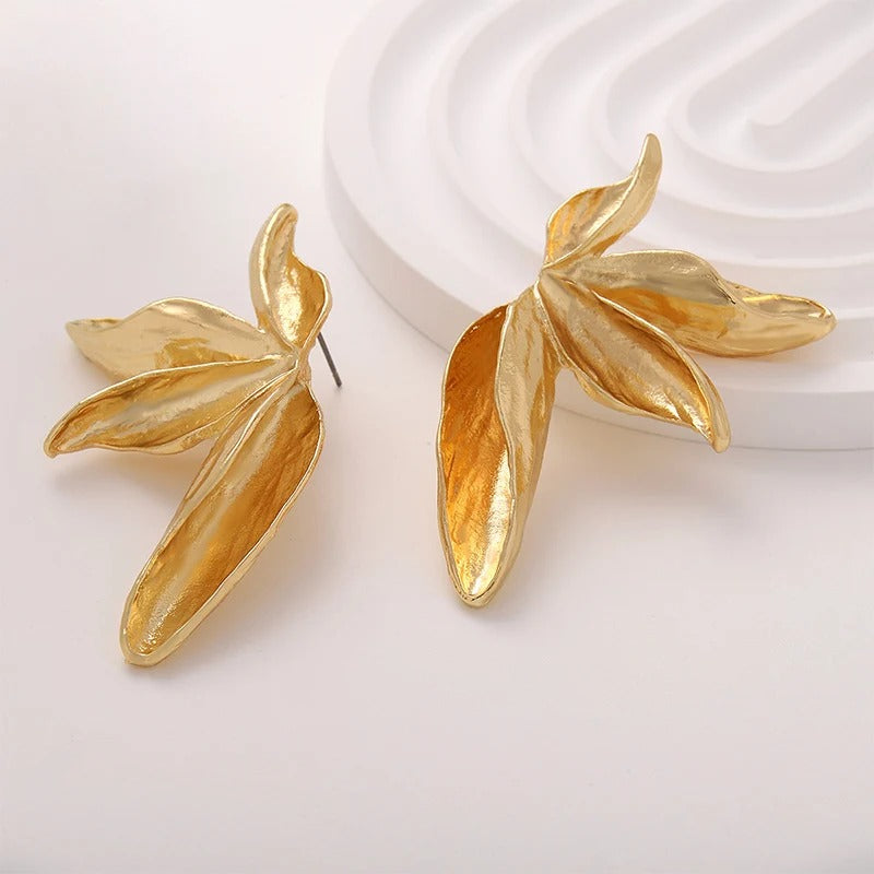 Gold leaf-shaped earrings on a light background